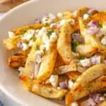 Cheese and chopped onions are scattered over a plate of Greek fries.