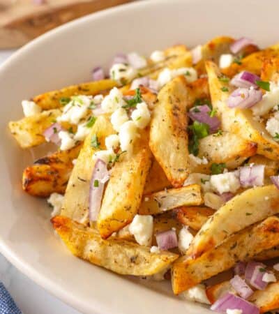 Cheese and chopped onions are scattered over a plate of Greek fries.