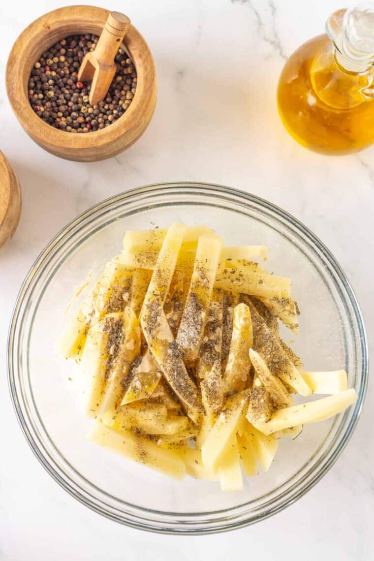 Herbs and salt and pepper are added to a bowl of potatoes.