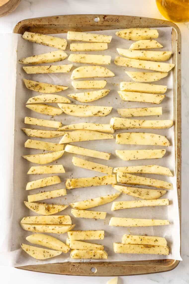 Seasoned fries are placed on a baking sheet.