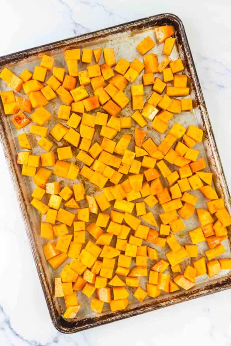 Cubed of raw butternut squash spread out on a baking sheet.