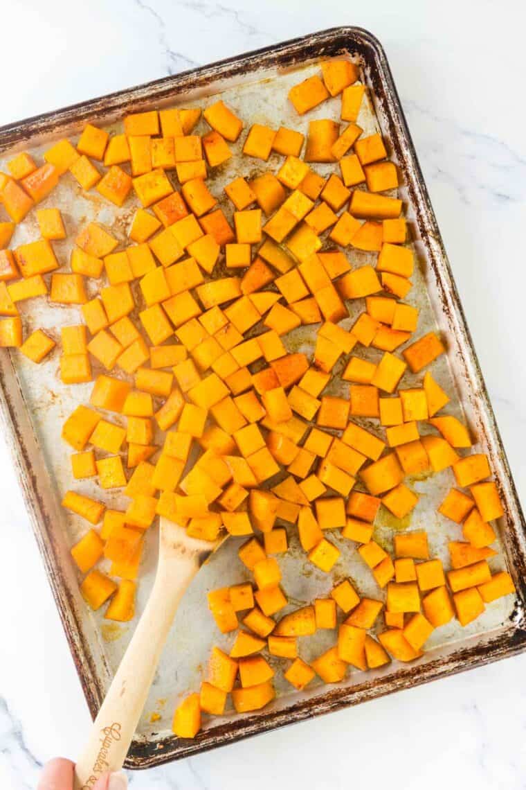 Tossing squash with a spatula on a sheet pan.