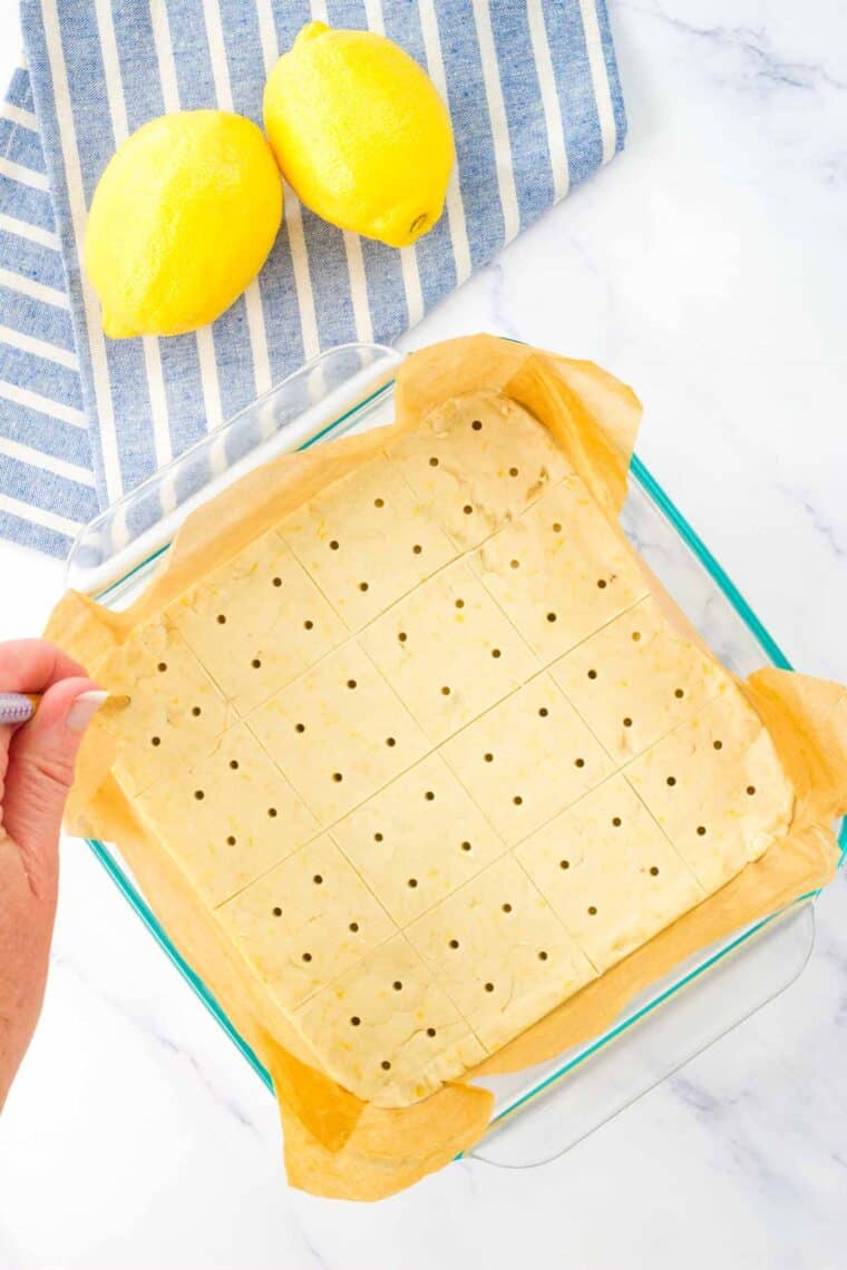 A tooth pick is used to prick the top of a pan of lemon shortbread dough.