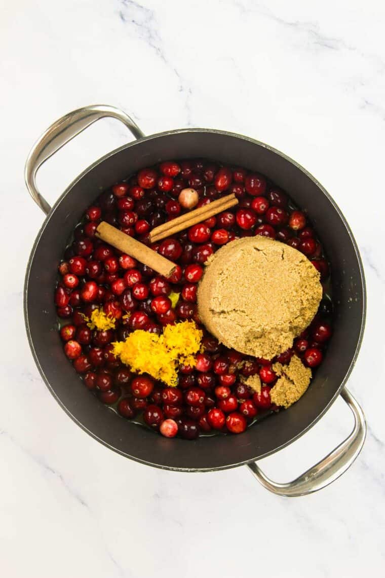 Cranberries in a pot with brown sugar and orange zest.