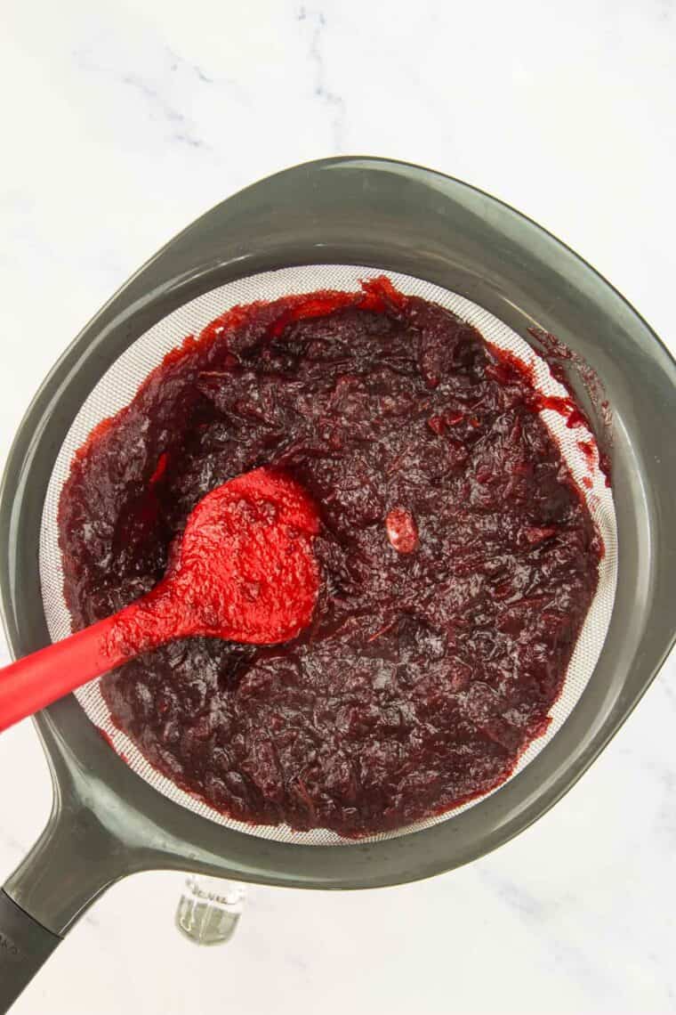 Straining the cranberry sauce in a mesh sieve.