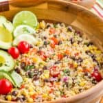 A wooden bowl of quinoa tossed with veggies and black beans with text overlay that says "Mexican Quinoa Salad".