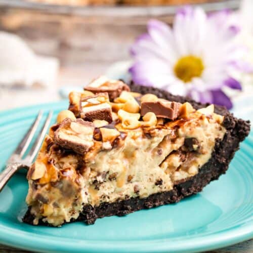 A big slice of snickers pie on a blue plate with a daisy.