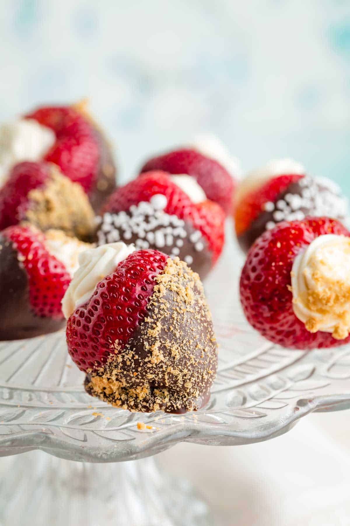 A glass cake plate with cheesecake stuffed strawberries dipped in chocolate.