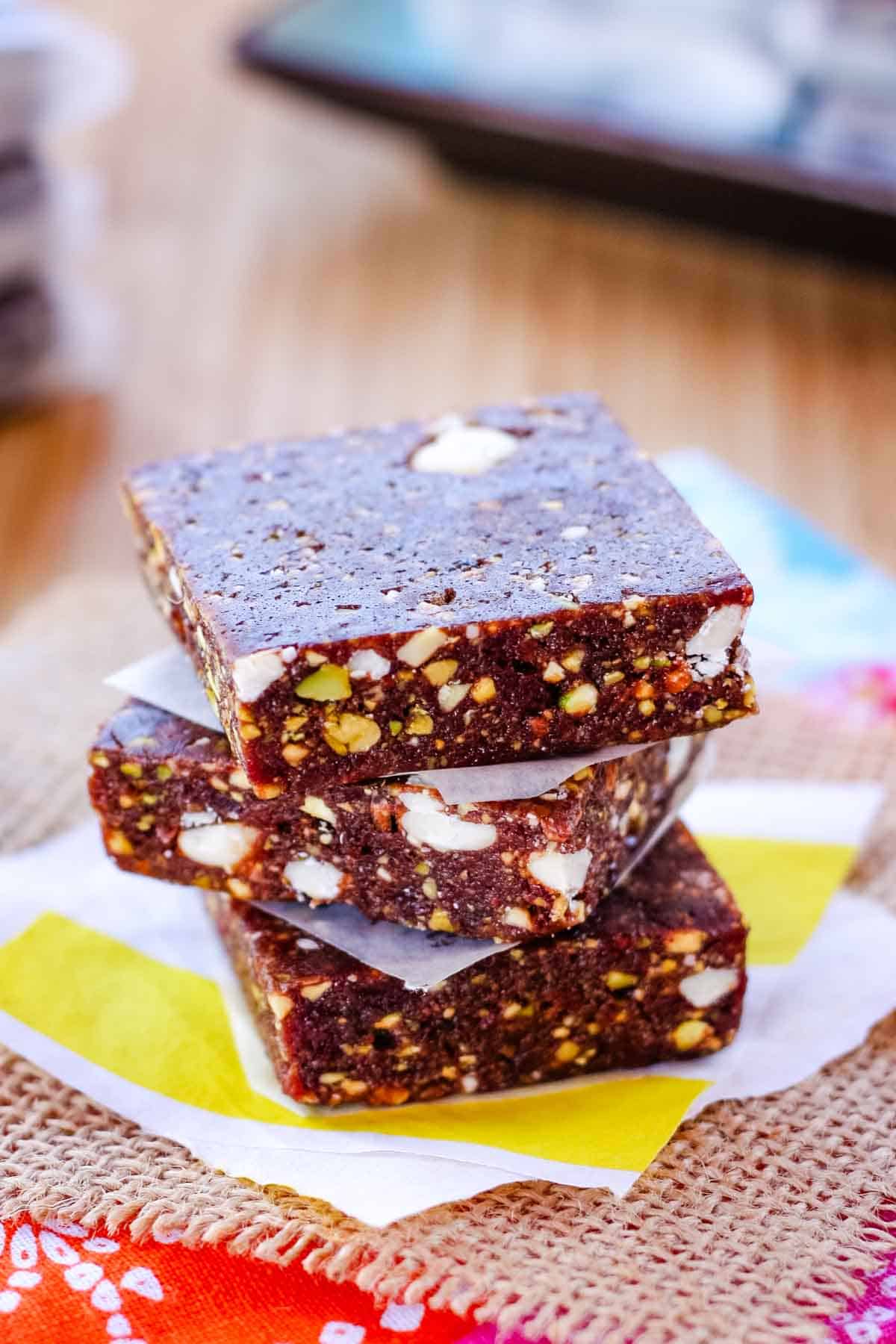 These 5-ingredient Cherry Energy Bars are my version of homemade Lara Bars and feature chewy bars dotted with pistachios and white chocolate. Three cherry energy bars stacked on top of each other.