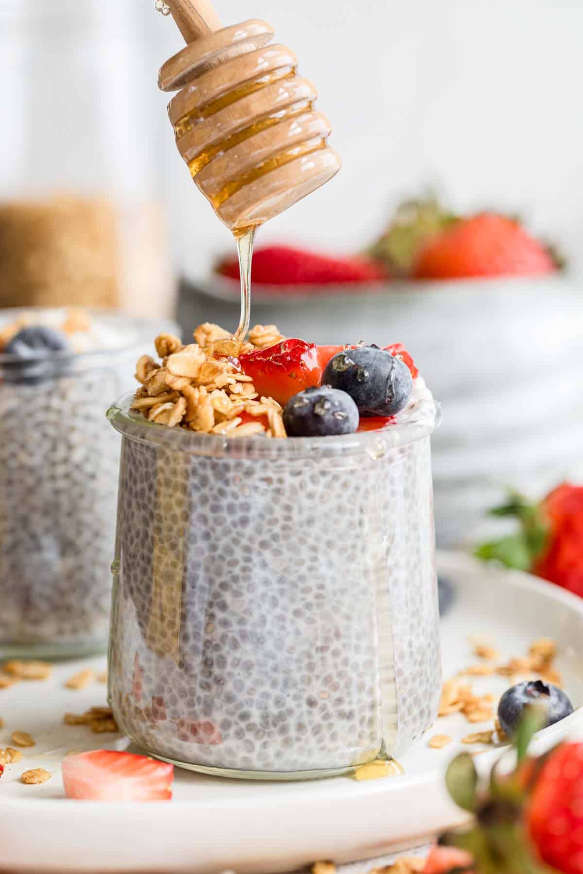 A honey stick drizzles honey over a glass jar of chia seed pudding.