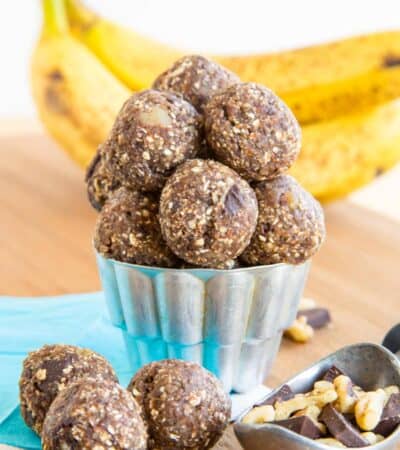 Bananas in the background of a container of Chunky Monkey banana energy balls.