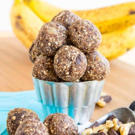 Bananas in the background of a container of Chunky Monkey banana energy balls.