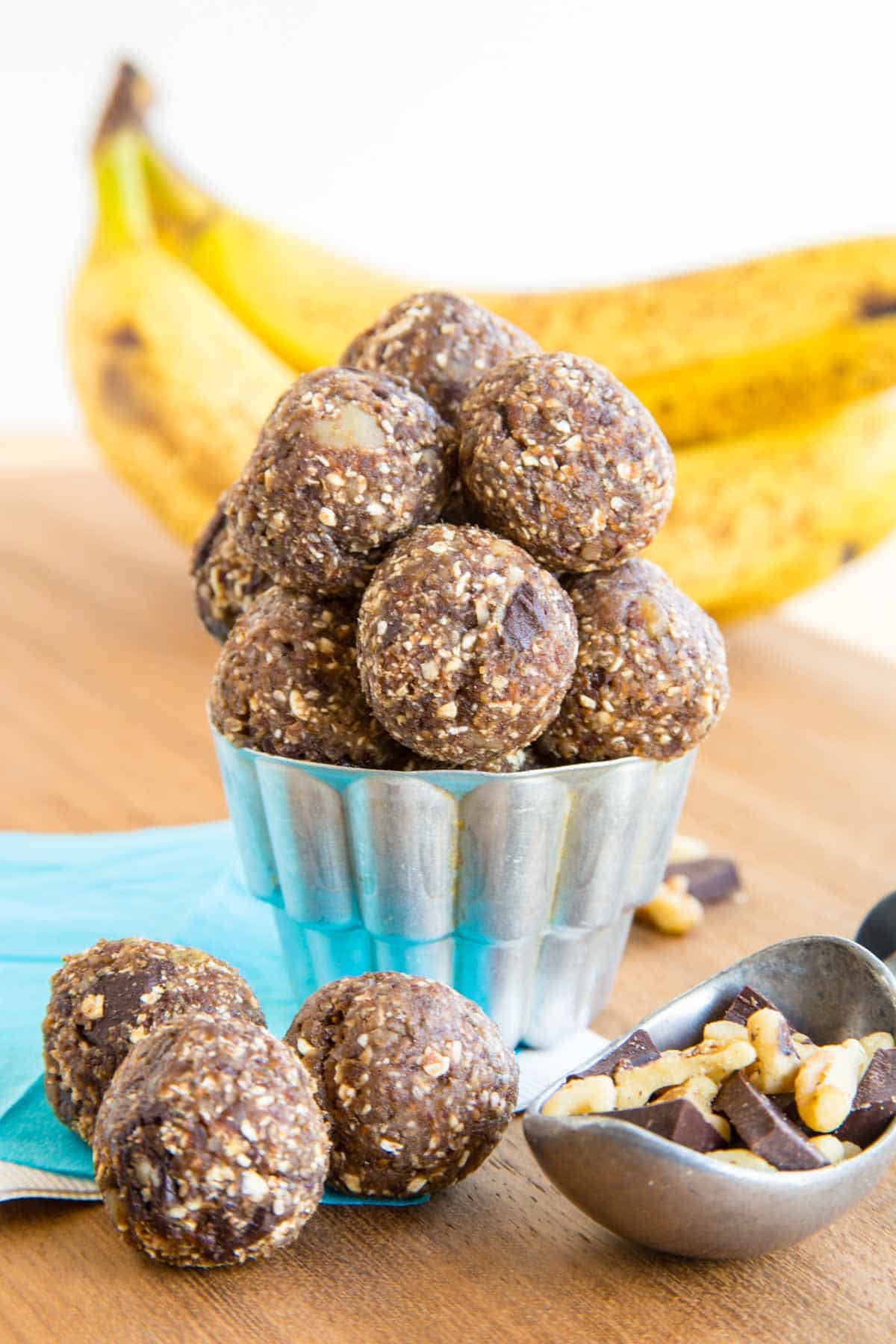 Bananas in the background of a container of Chunky Monkey banana energy balls.