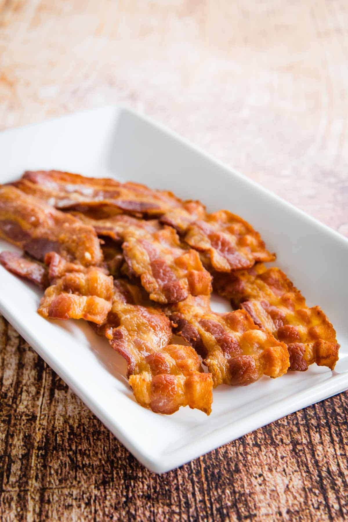 Cooked crispy bacon slices on a white plate.