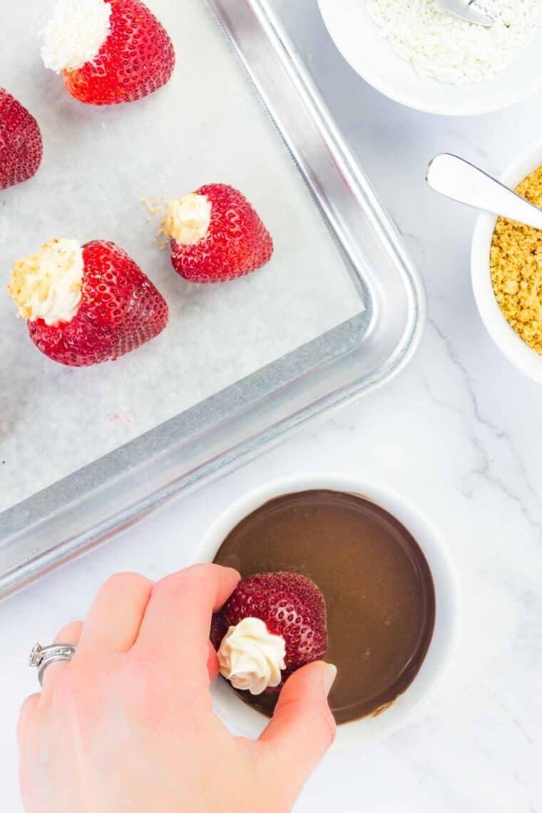 A hand dips a stuffed strawberry in melted chocolate.