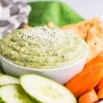 A bowl of a green-colored dip surrounded by a dish of veggies with text overlay that says "Parmesan White Bean Dip".