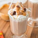 A glass mug of hot cocoa topped with whipped cream and chopped Reese's with text overlay that says "Peanut Butter Hot Chocolate".