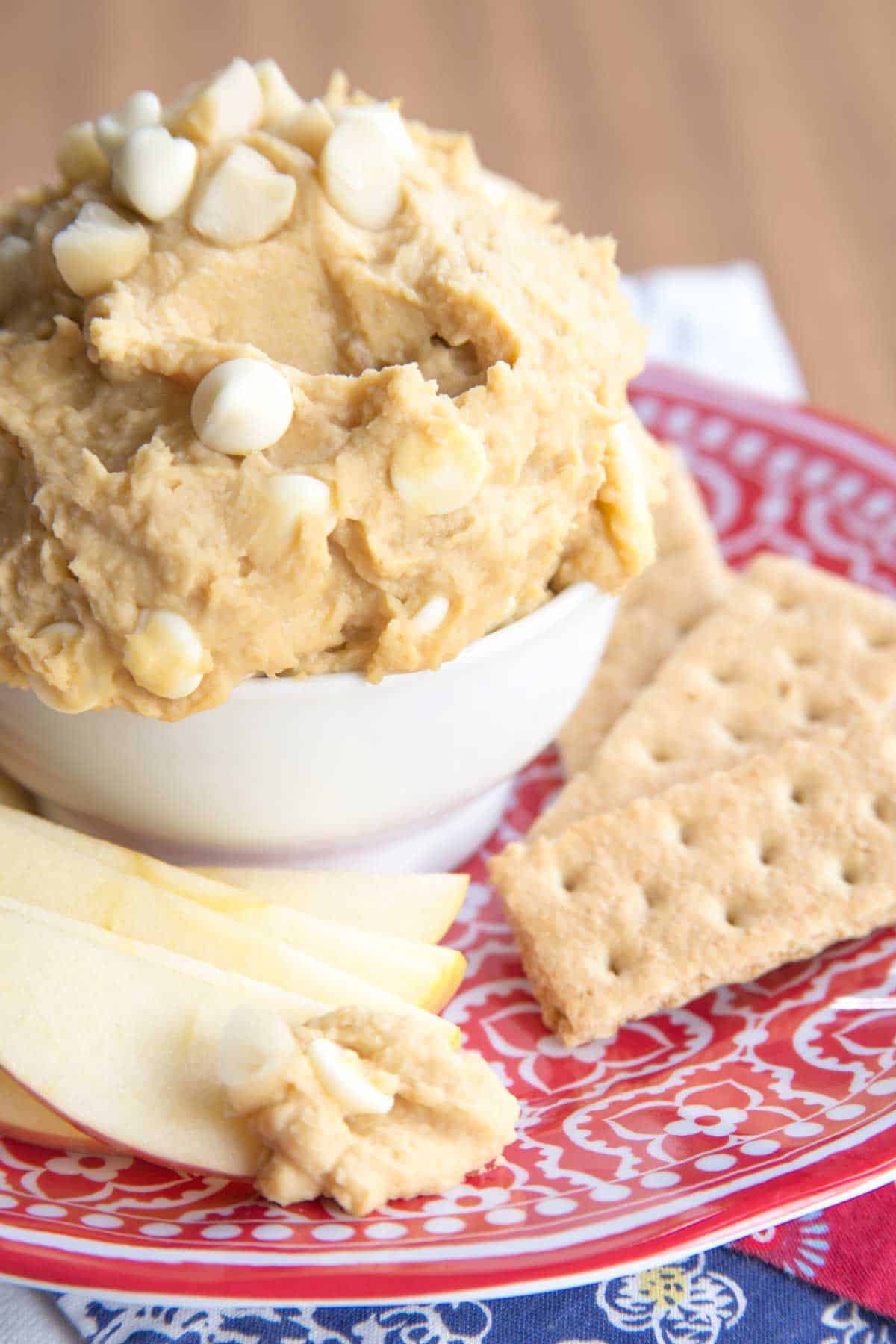 Cookies and apple slices next to a bowl of white chocolate macadamia nut cookie dough dip.