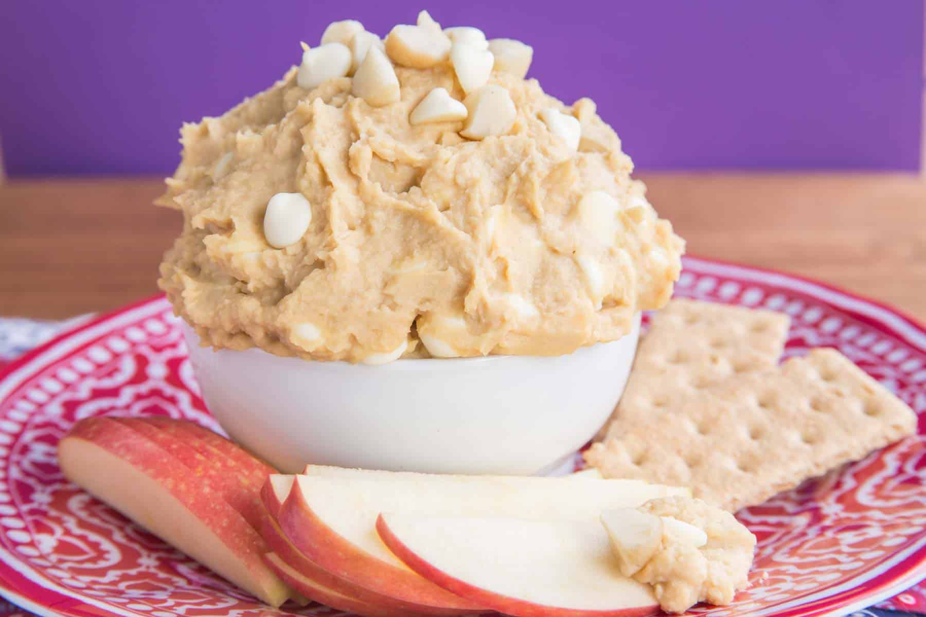Cookies and apple slices next to a bowl of white chocolate macadamia nut cookie dough dip.
