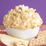 An apple slice next to white chocolate macadamia nut cookie dough dip.
