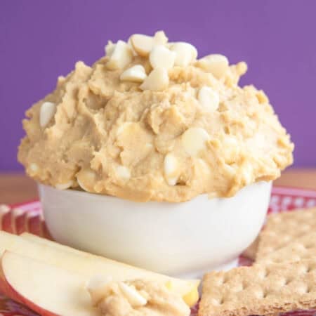 An apple slice next to white chocolate macadamia nut cookie dough dip.