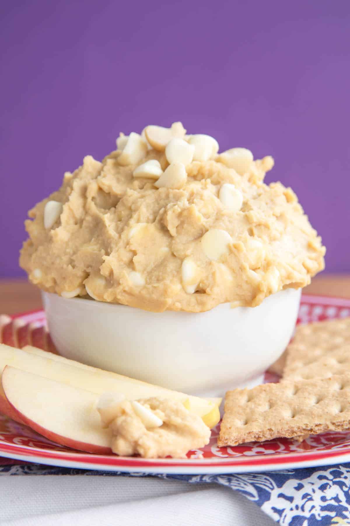White chocolate macadamia nut Cookie Dough Dip is a dippable, egg and gluten-free take on a classic cookie! An apple slice next to white chocolate macadamia nut cookie dough dip.