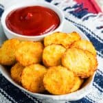 A serving tray with cauliflower tots and a bowl of ketchup.