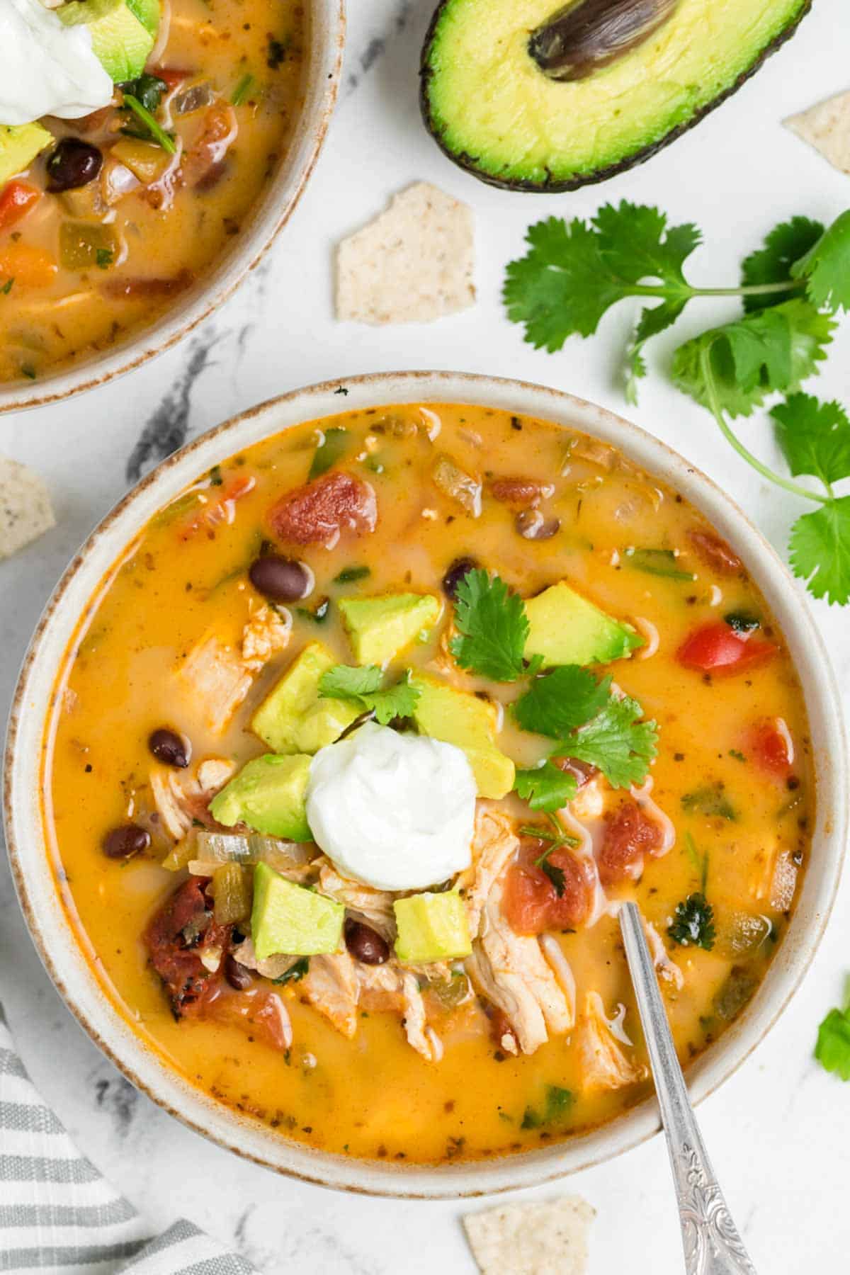 A bowl of chicken taco soup topped with avocado and sour cream.