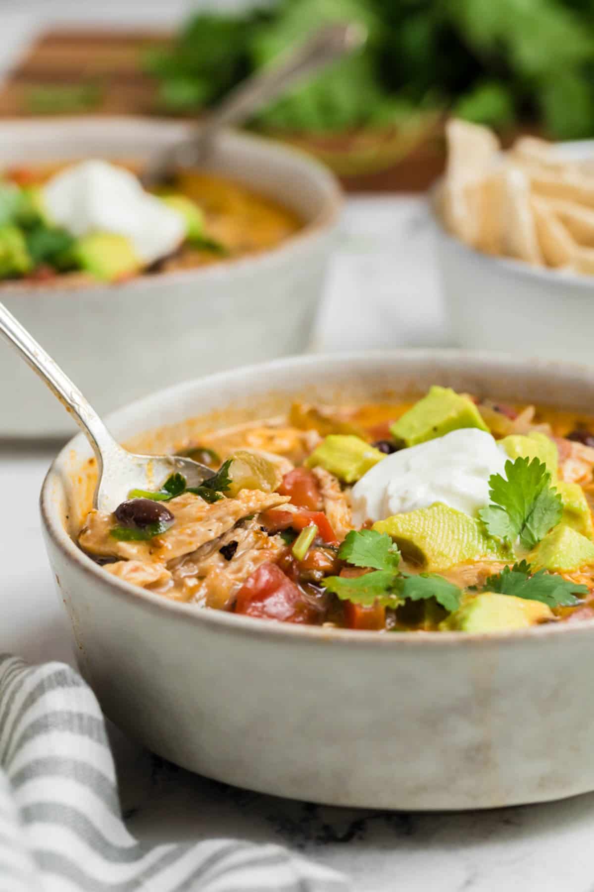 Two bowl of chicken soup with spoons on a table.