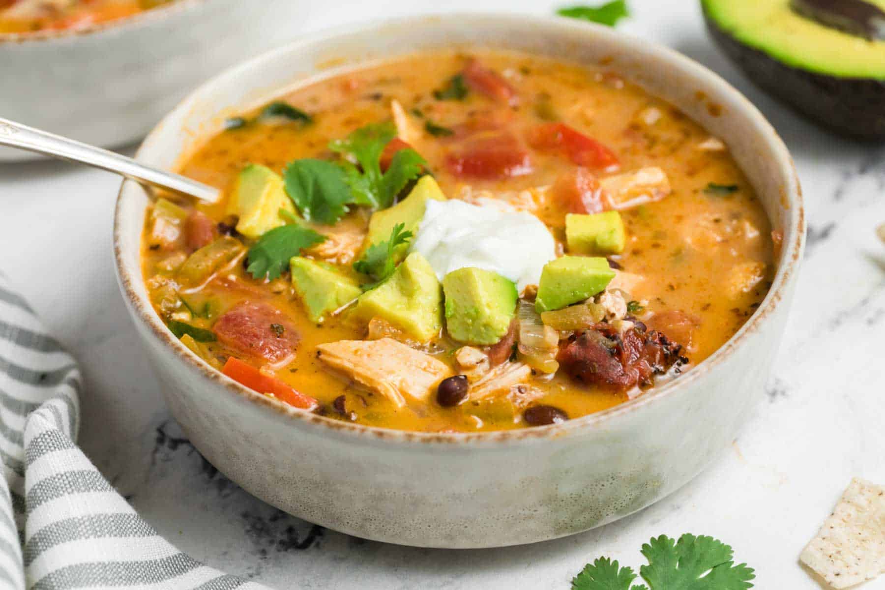 A bowl of chicken taco soup topped with avocado and sour cream.