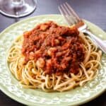 A wine glass next to a plate of pasta with chickpeas in tomato sauce.
