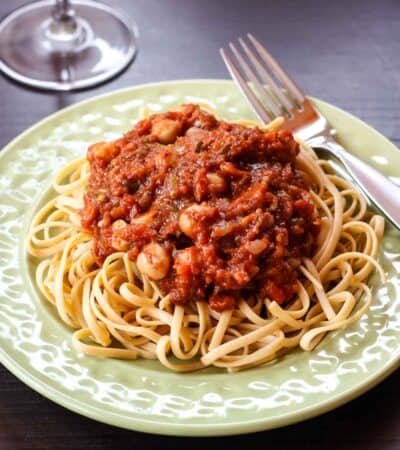 A wine glass next to a plate of pasta with chickpeas in tomato sauce.