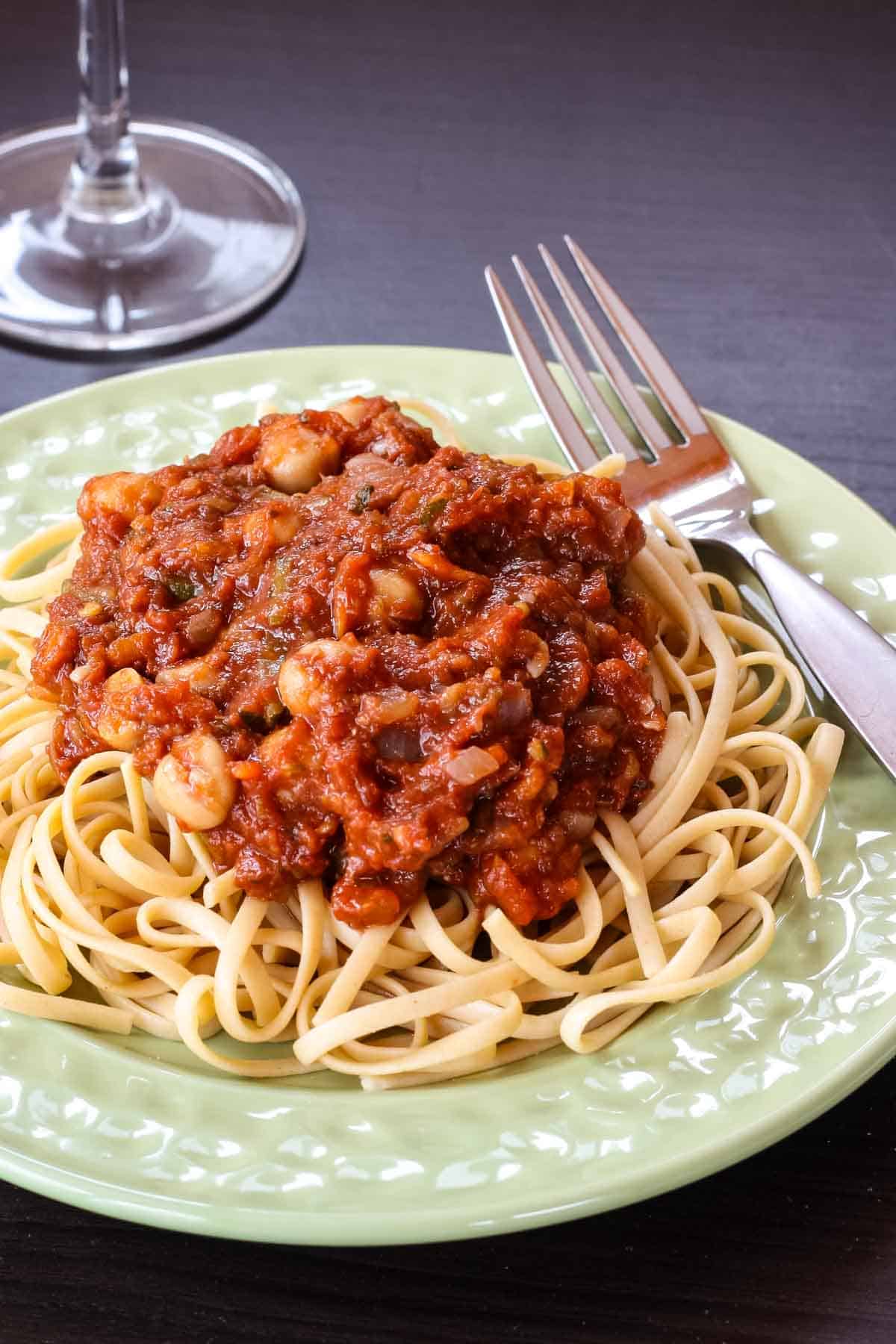 A rich, flavorful pasta sauce packed with veggies and protein, that comes together fast for a satisfying weeknight meal. A fork rests on a plate of chickpeas in tomato sauce.