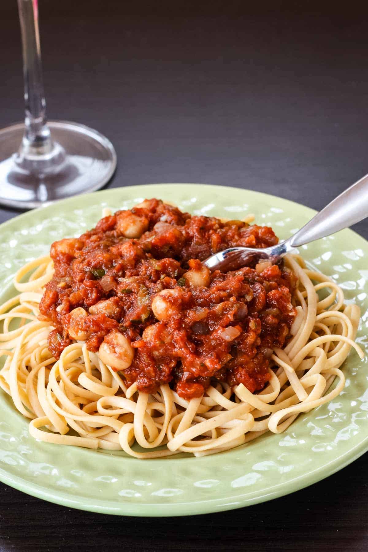 A fork in a plate of pasta topped with chickpeas and tomato sauce.
