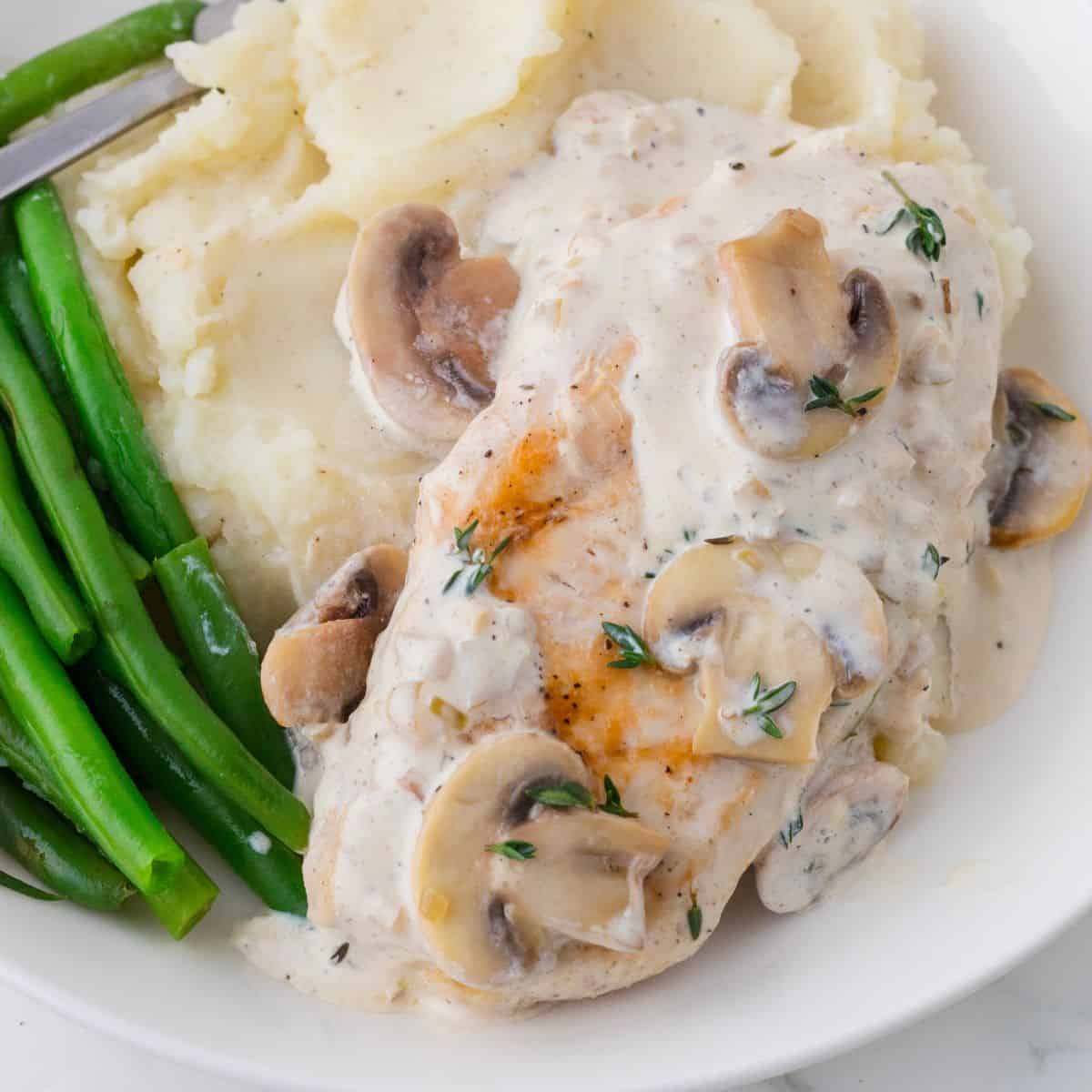 Creamy mushroom chicken on a plate with green beans and mashed potatoes.