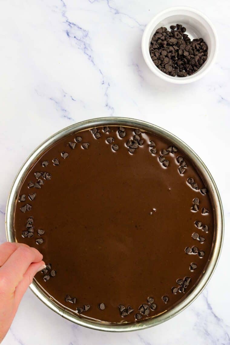 Chocolate chips are added to the ganache on top of cheesecake.