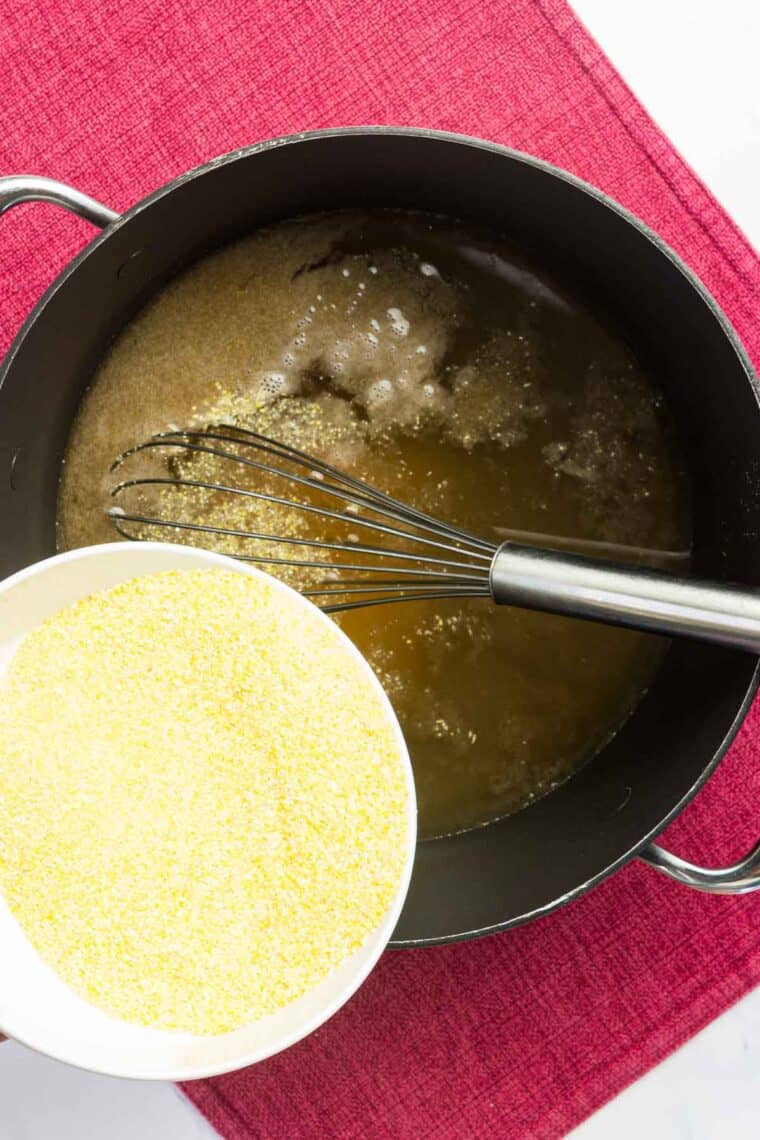 Cornmeal being poured into a pot of chicken broth.