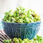A blue bowl filled with green popcorn and more popcorn scattered around it.