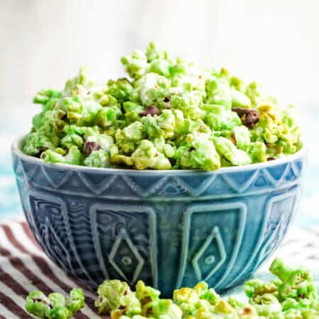 A blue bowl filled with green popcorn and more popcorn scattered around it.