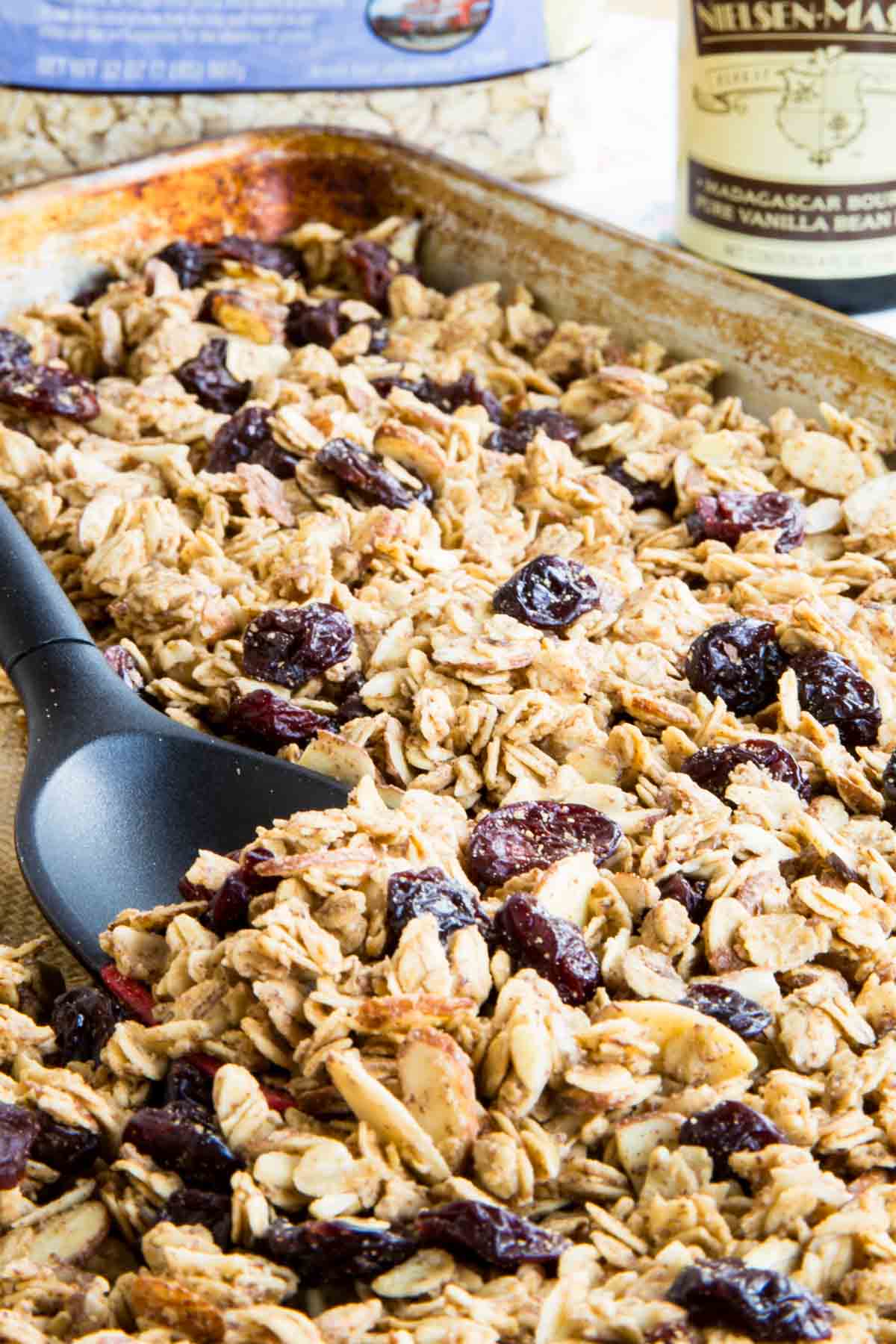 A spoon stirs a tray of almond granola.
