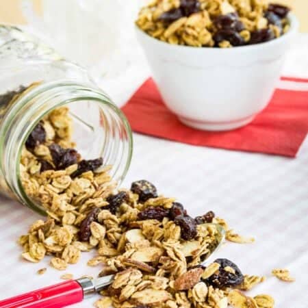 Almond granola spills out of a jar with a bowl of granola behind it.