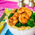 A bowl of cheesy quinoa topped with broccoli and shrimp with text overlay that says "BBQ Shrimp Quinoa Bowls".