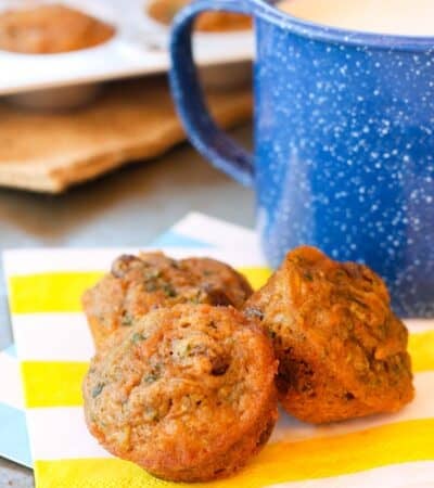 Three carrot zucchini muffins next to a blue mug,