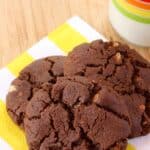 Three chocolate cookies on a yellow and white striped napkin with text overlay that says "Flourless Chocolate Almond Cookies".