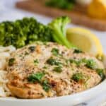 A cooked piece of chicken with parsley on a plate with text overlay that says "Garlic Butter Chicken".