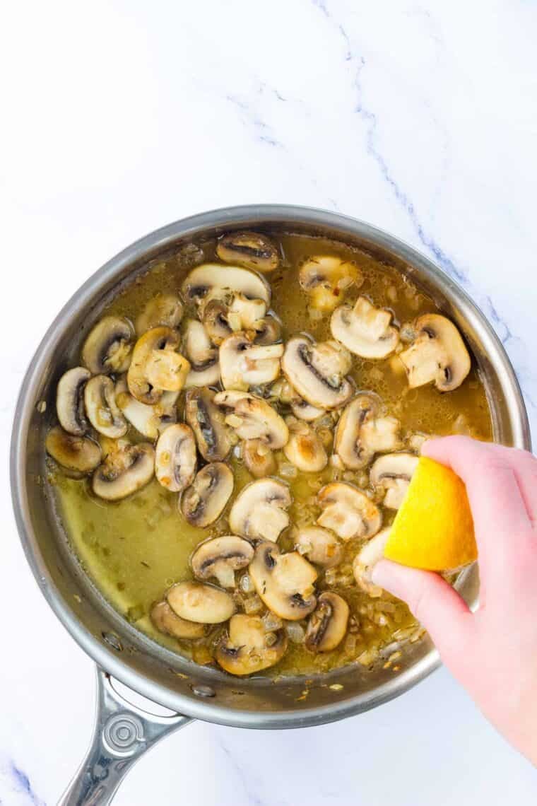 Lemon juice is squeezed onto a skillet of mushrooms.