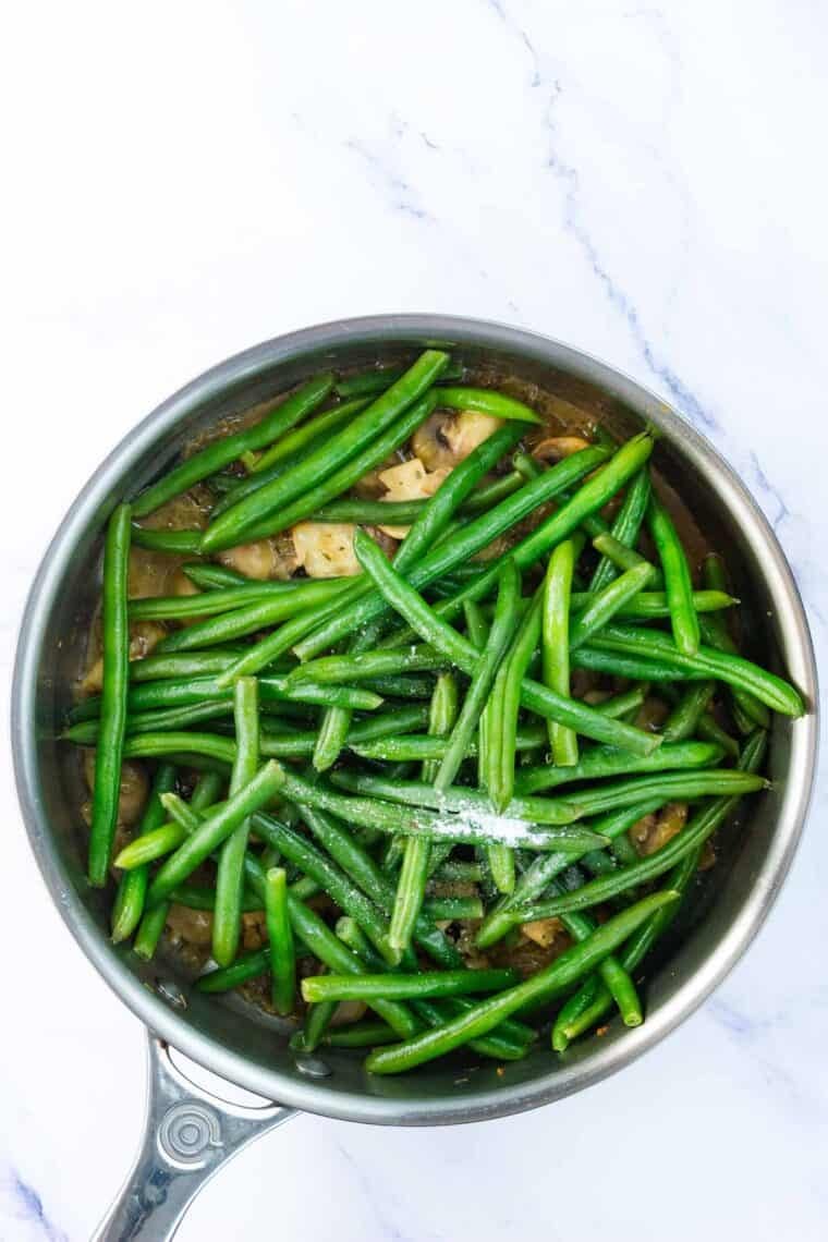 Green beans are added to a skillet of mushrooms.