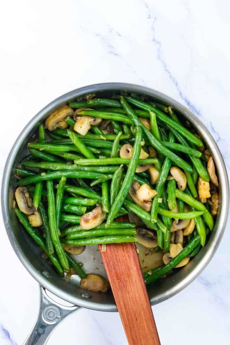 A wooden spoon stirs a skillet of green beans.