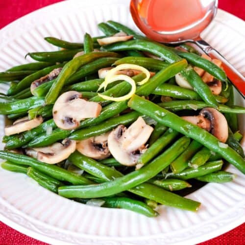 A plate of green beans and mushrooms with a little dish of sauce.