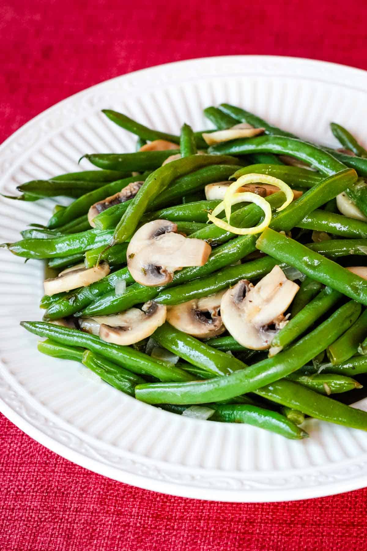 A white plate with sauteed green beans and mushrooms on a red backgrounf.